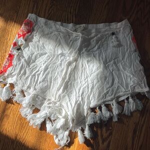 White fabric shorts with neon coral pattern on sides and tassels.